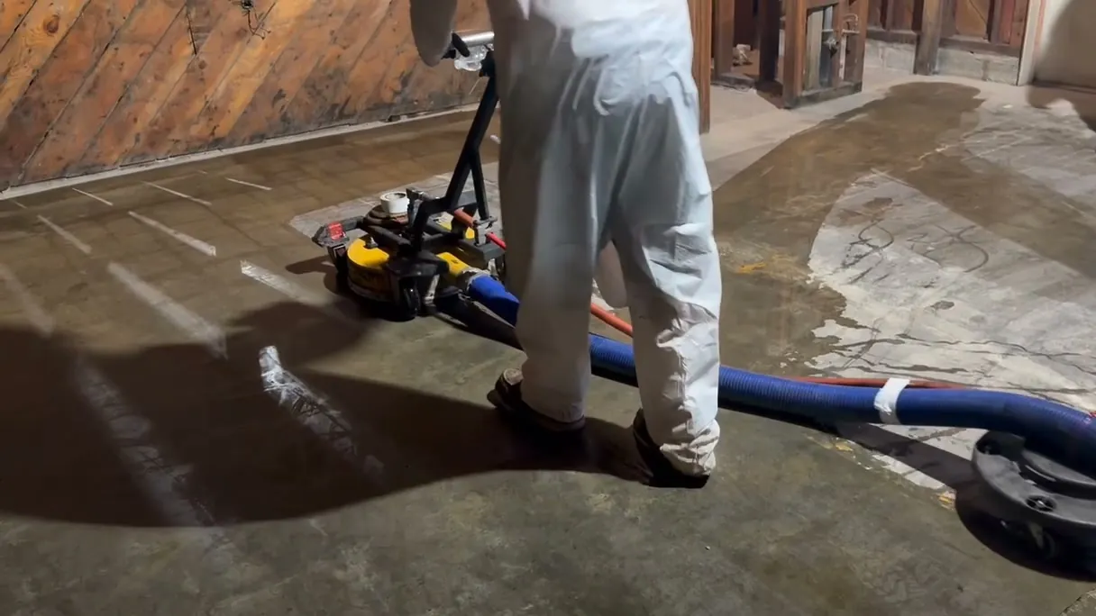Worker in a white protective suit running a UHP floor unit over a stripped concrete floor during an interior job